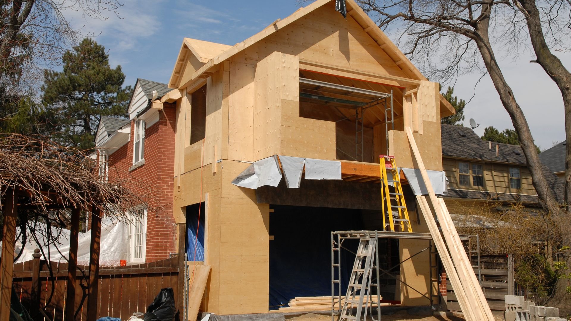 Two-story home addition under construction with wooden framing and ladders