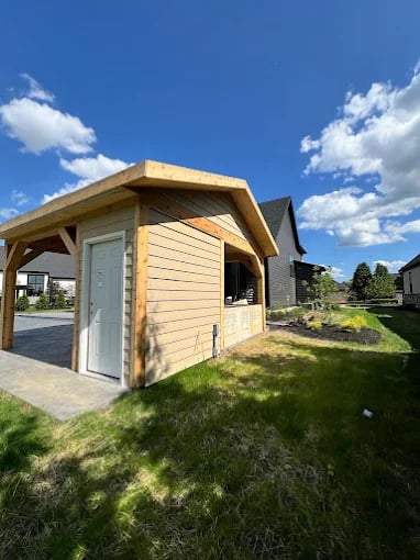 Wooden shed with white door in sunny backyard with green grass