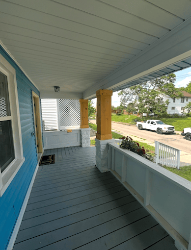 Wooden porch with blue siding, white columns, and view of driveway