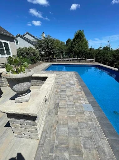 Backyard swimming pool with stone patio and landscaped surroundings