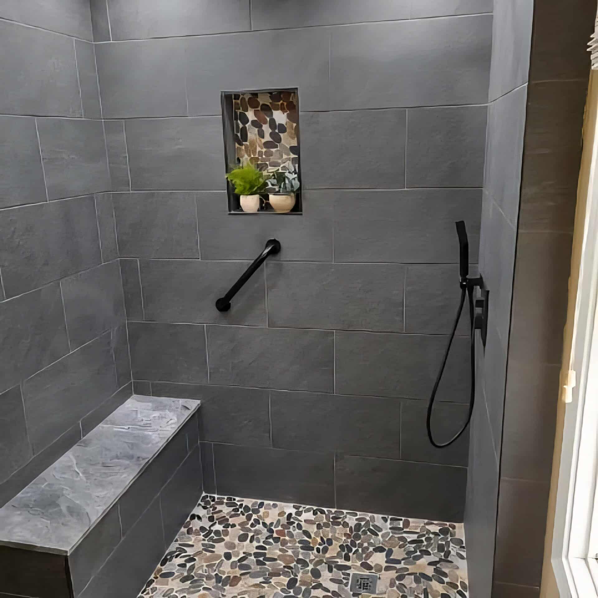 Modern gray shower with stone floor, black fixtures, and green plant