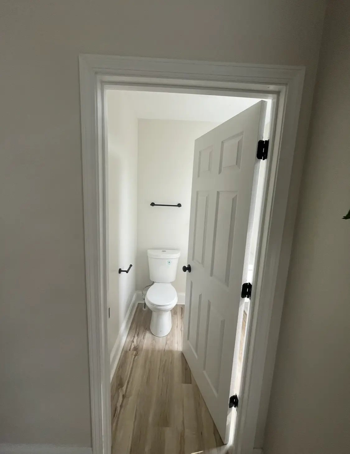 White toilet in narrow bathroom with wooden floor and open door