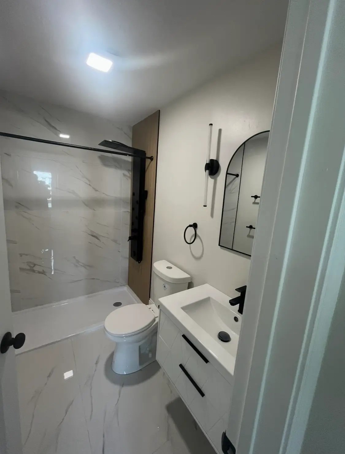 Modern white bathroom with marble tiles, shower, and black fixtures
