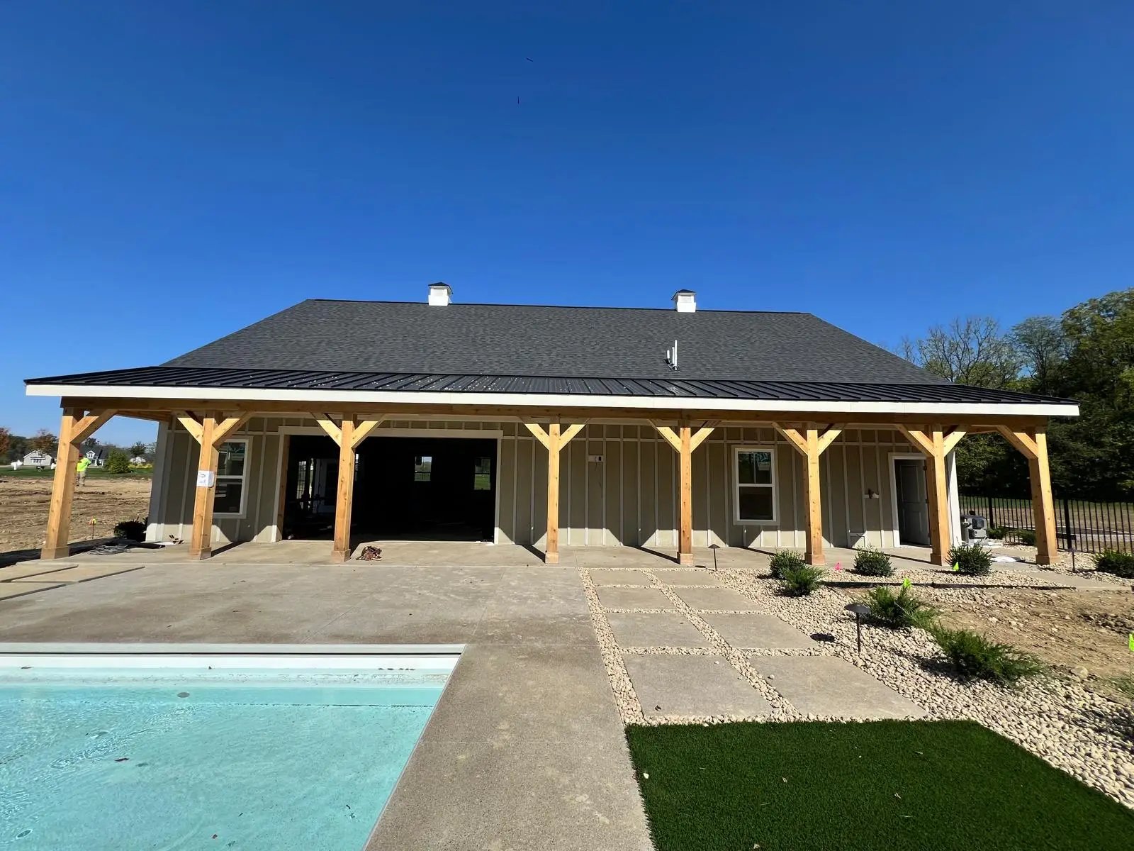 Modern barn-style building with wooden posts and pool on sunny day
