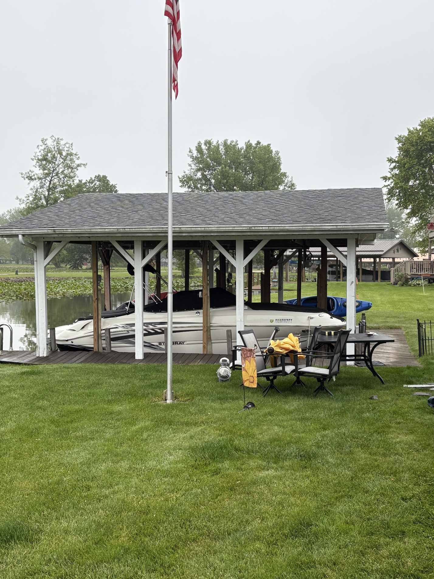 Boat docked under wooden shelter near pond with American flag