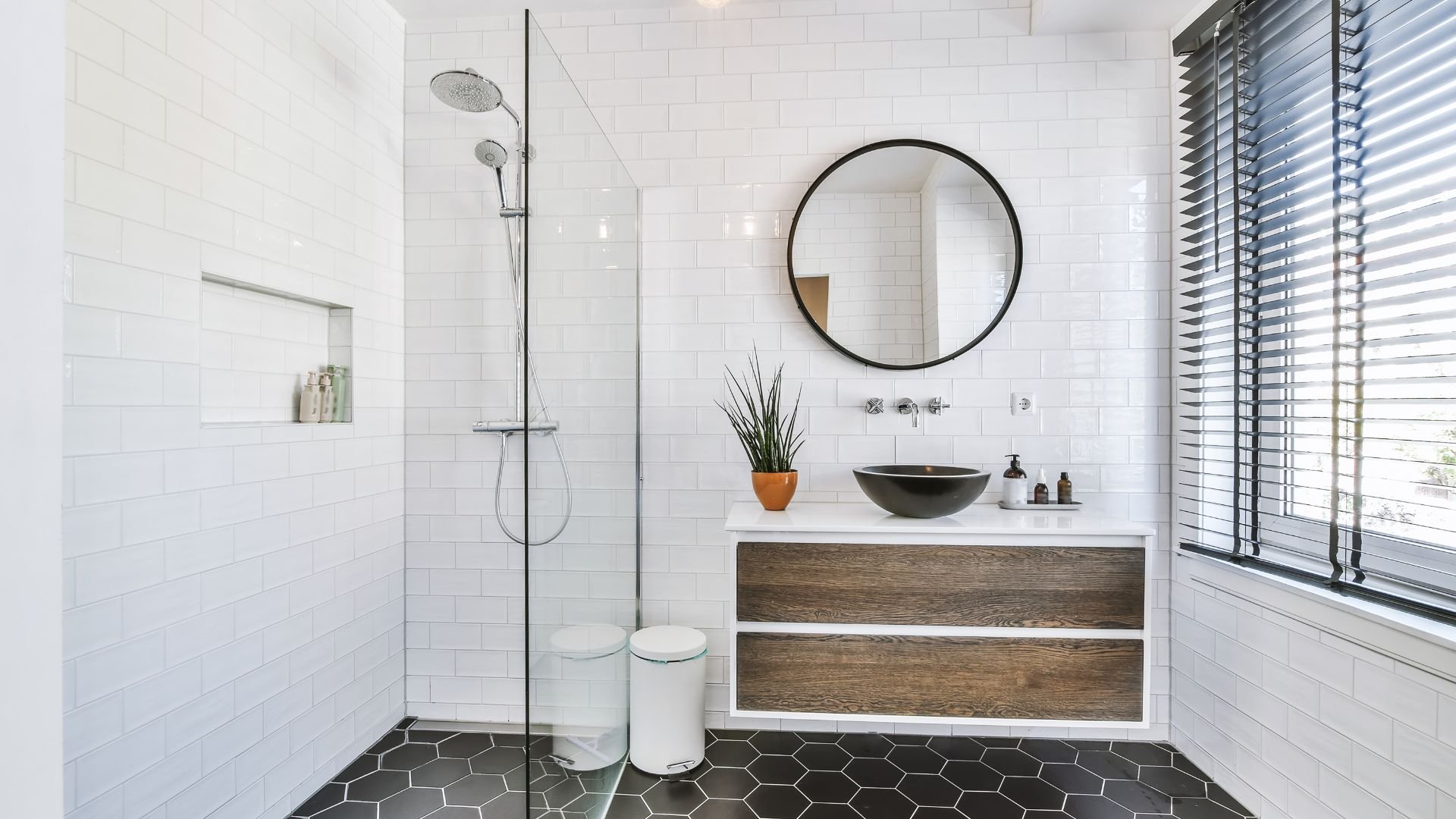 Modern white bathroom with glass shower, round mirror, and wooden vanity