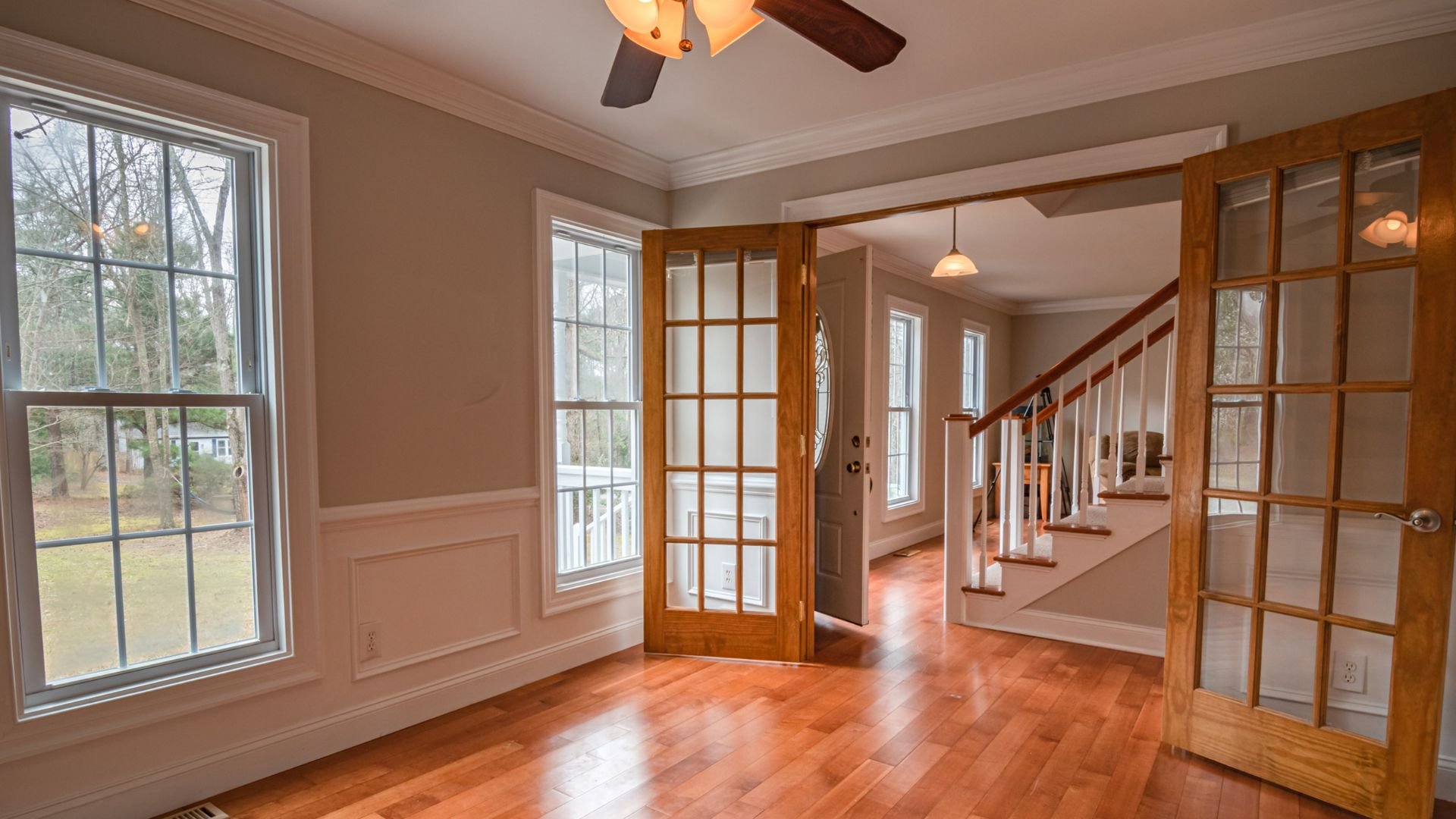 Bright empty room with hardwood floors, windows, and staircase