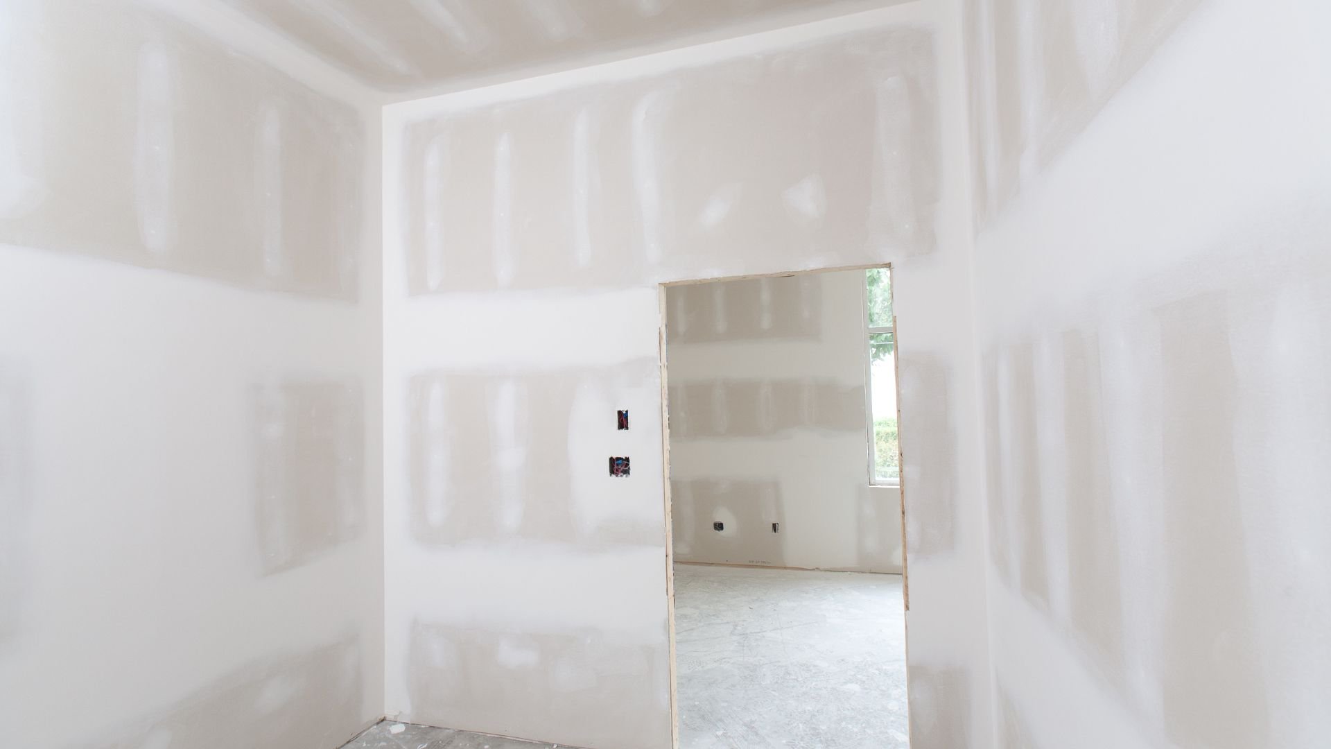 Unfinished room with drywall, open doorway, and window showing trees
