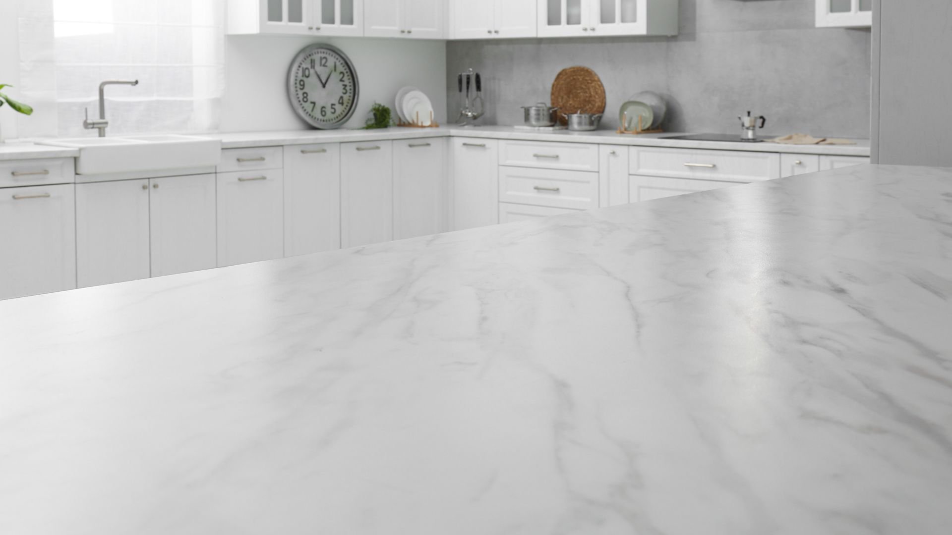 Clean white kitchen with marble countertop and wall clock